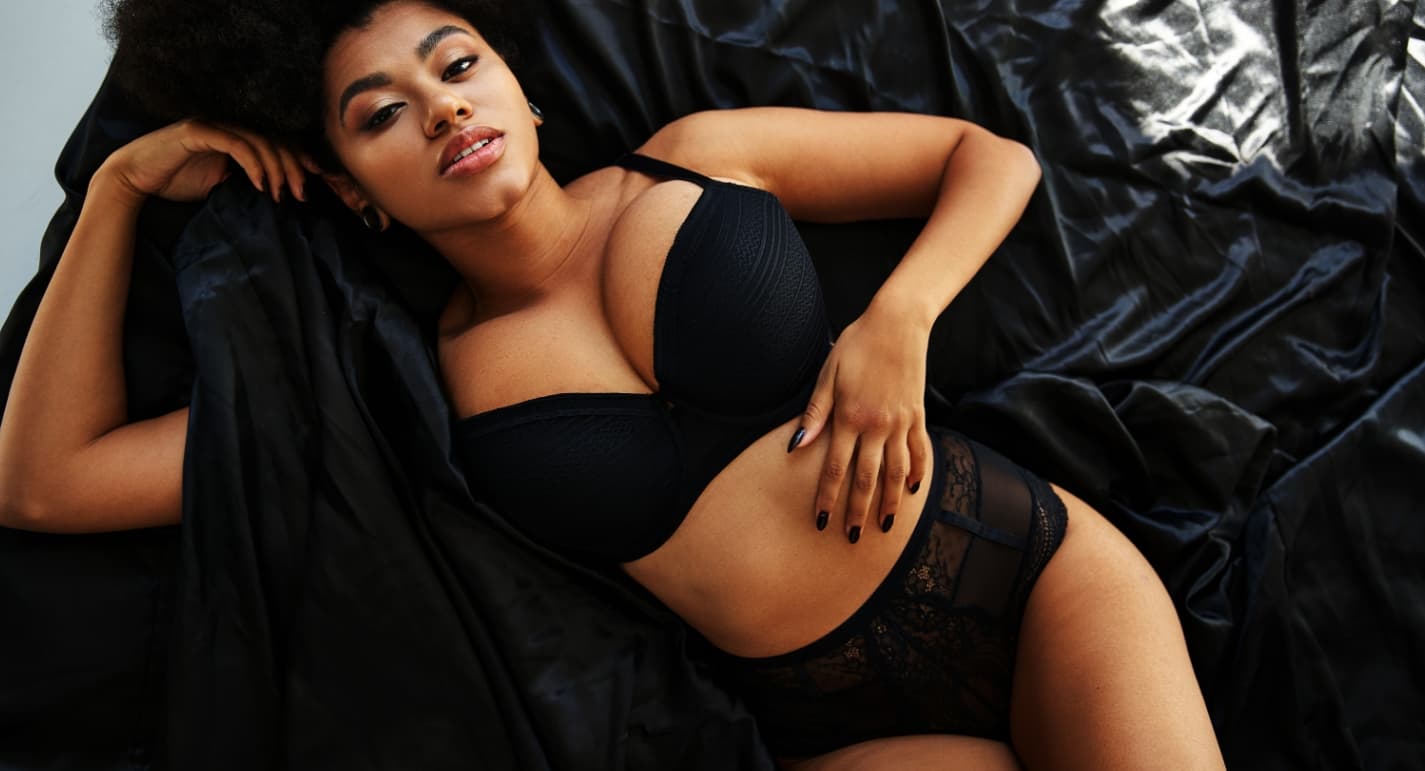 A curvy woman laying on a bed on her back in black lingerie